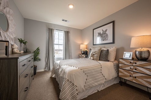 Interior photo of guest bedroom with bed, dresser, and large window.