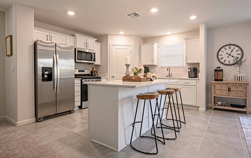 Interior photo of kitchen with white cabinets, white countertops, stainless steel appliances, and barstools at kitchen island.