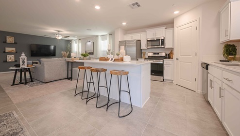 Interior photo of kitchen with white cabinets, white countertops, stainless steel appliances, and barstools at kitchen island.