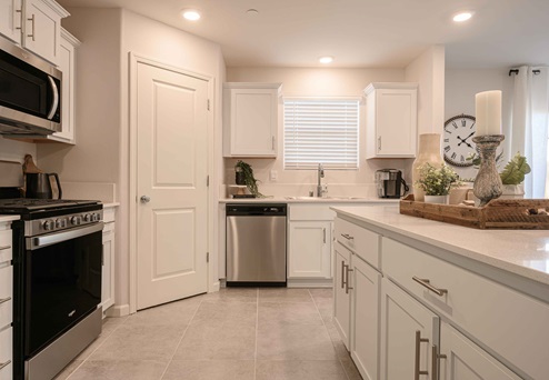 Interior photo of kitchen with white cabinets, white countertops, stainless steel appliances, and large window.