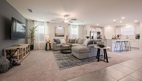 Interior photo of living room with large couch, coffee table, TV, and large windows.