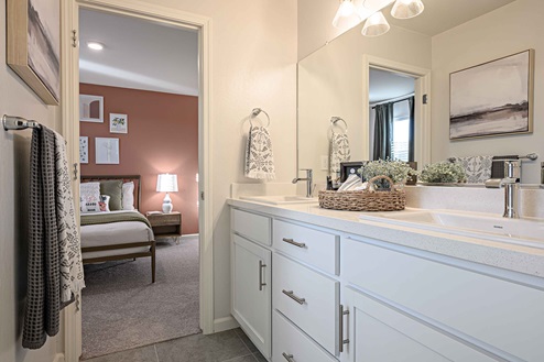 Interior photo of Jack and Jill bathroom with white cabinets, white countertops, and large mirror.