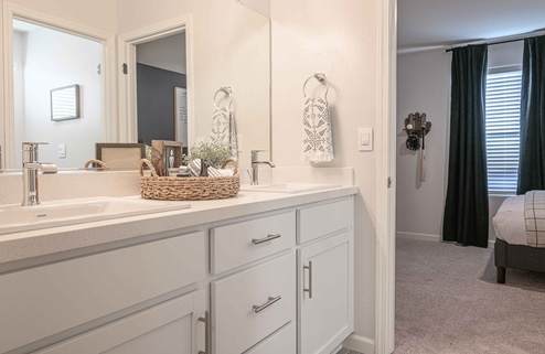 Interior photo of Jack and Jill bathroom with white cabinets, white countertops, and large mirror.