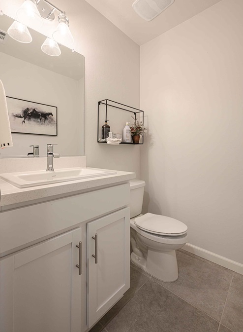 Interior photo of guest bathroom with white cabinets, white countertop, toilet, and large mirror