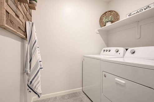 Interior photo of laundry room with washer, dryer, and shelf for storage.
