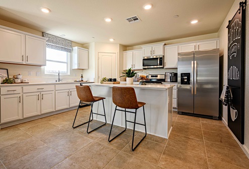 Interior photo of kitchen with white cabinets, white counter tops, and barstools at kitchen island