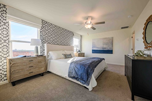 Interior photo of primary suite with bed, end tables, dresser, and large windows.