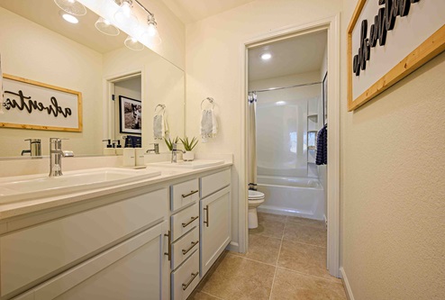 Interior photo of guest bathroom with white countertops, white cabinets, and a large mirror