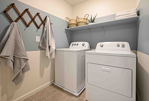 Interior photo of laundry room with washer, dryer, and shelf for storage.