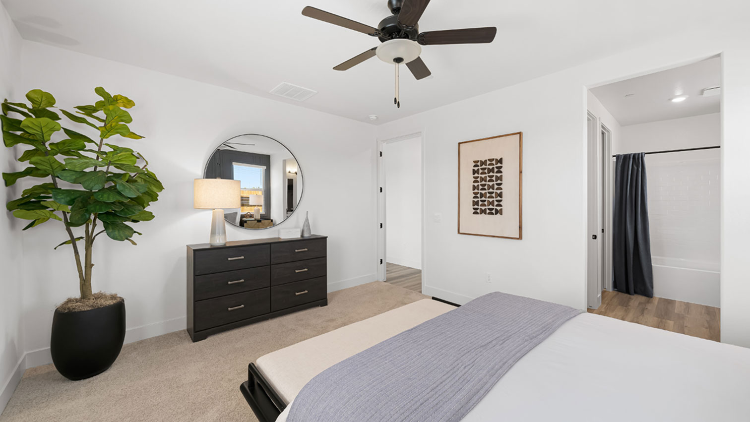 Primary bedroom with plush carpeting, ceiling fan, and dresser area
