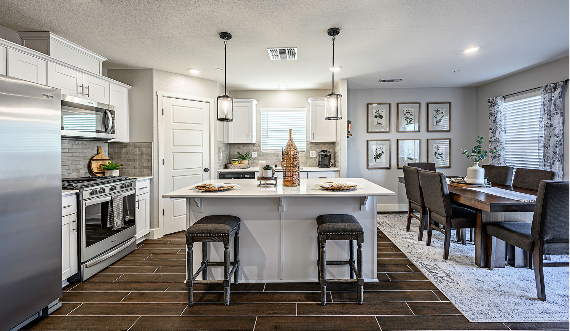 Interior photo of kitchen with white countertops, white cabinets, stainless steel appliances, and two barstools at kitchen island.