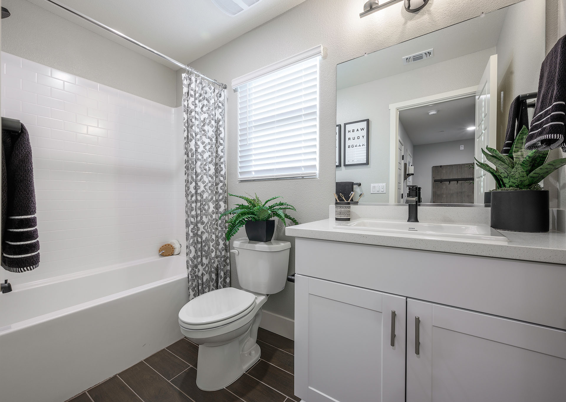Interior photo of guest bathroom with white cabinets, white countertops, shower, and large mirror.