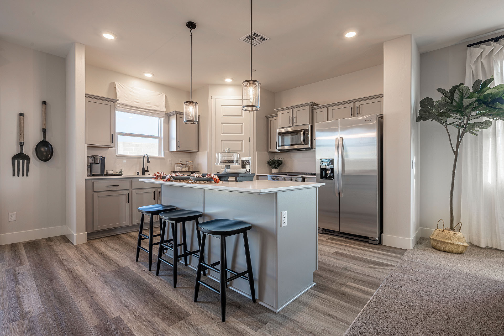 Interior photo of a kitchen with white countertops, white cabinets, stainless steel appliances, and barstools at kitchen island.