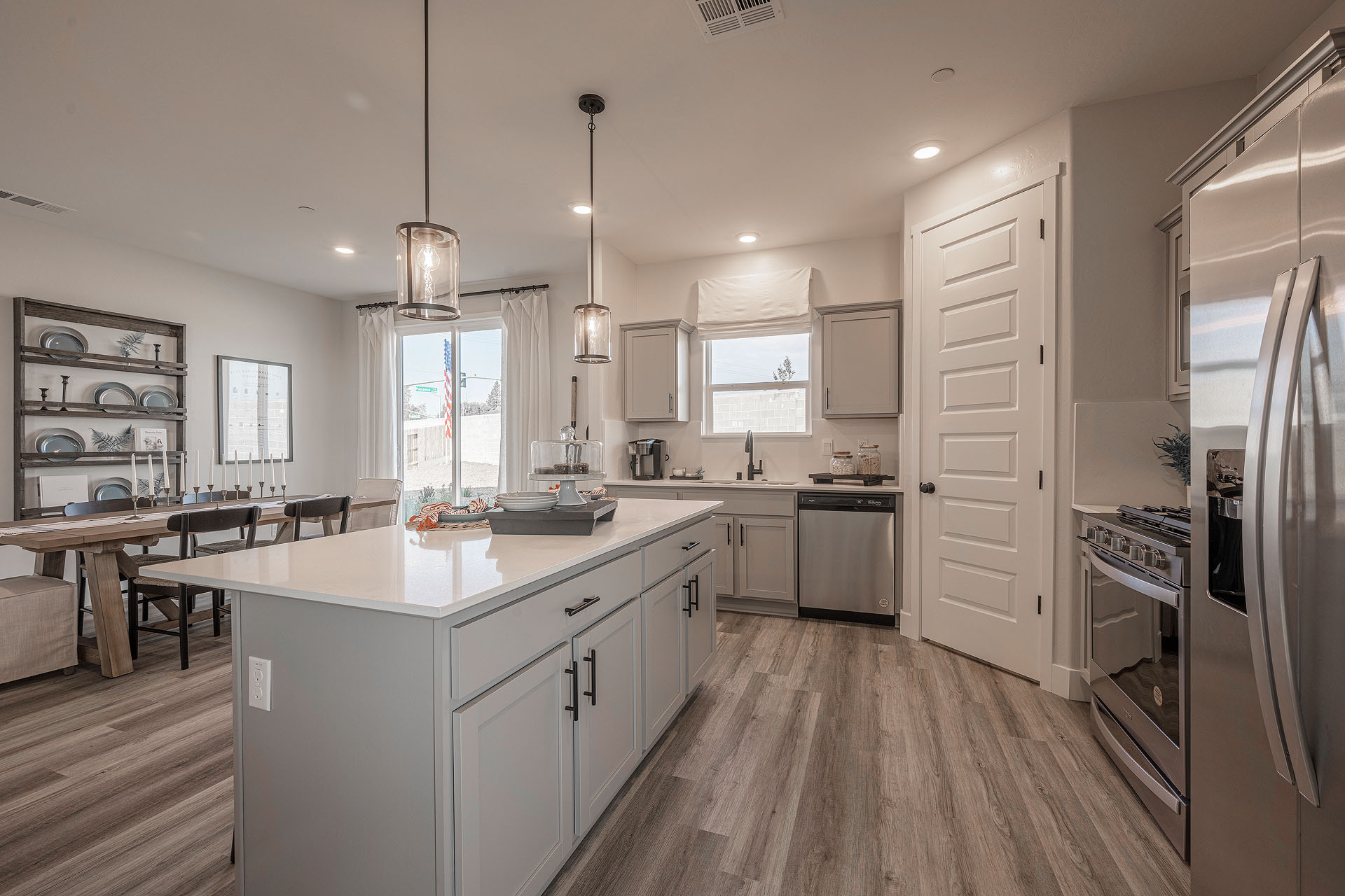 Interior photo of a kitchen with white countertops, white cabinets, stainless steel appliances, and barstools at kitchen island.