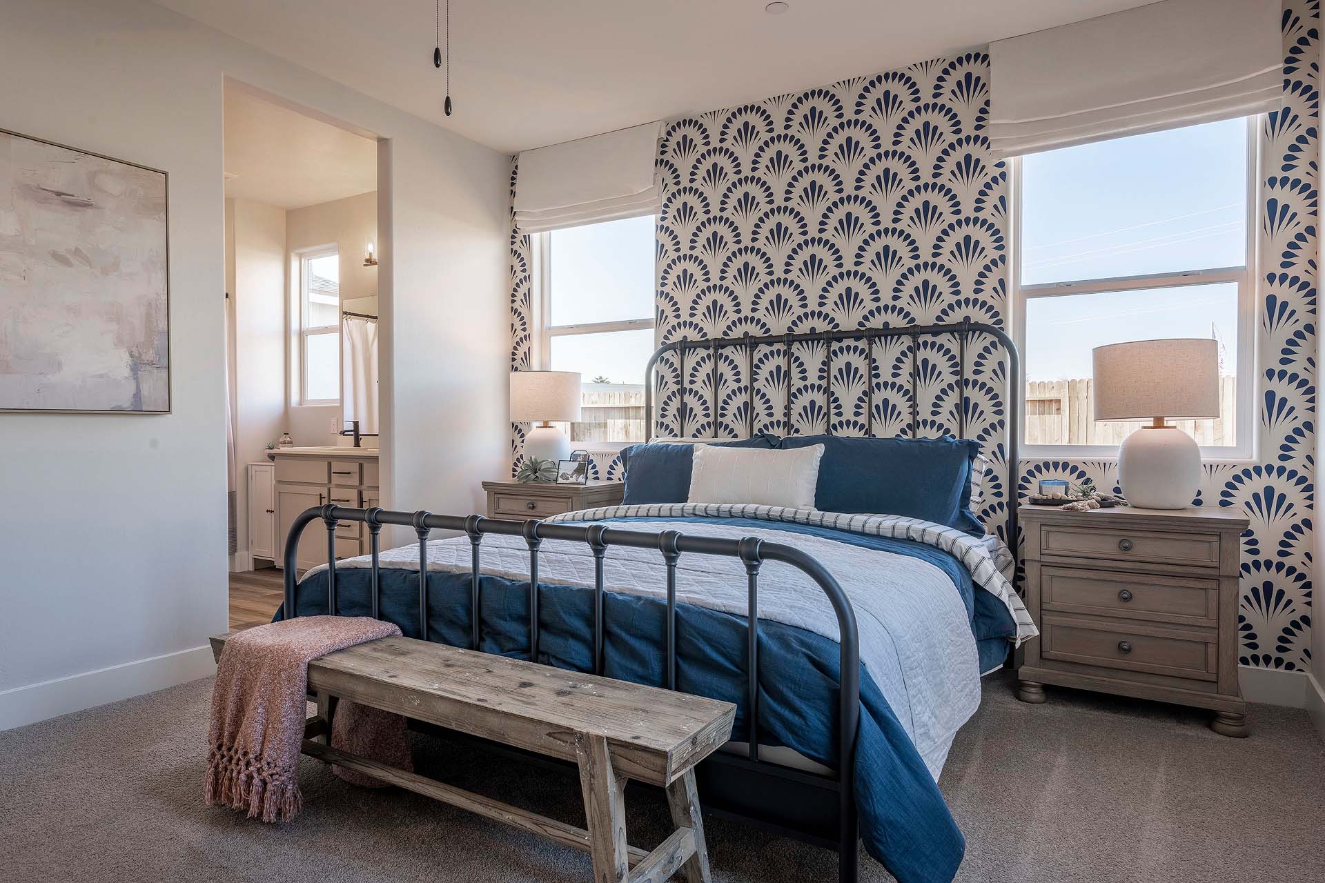 Interior photo of primary suite with bed, end tables, and two large windows.