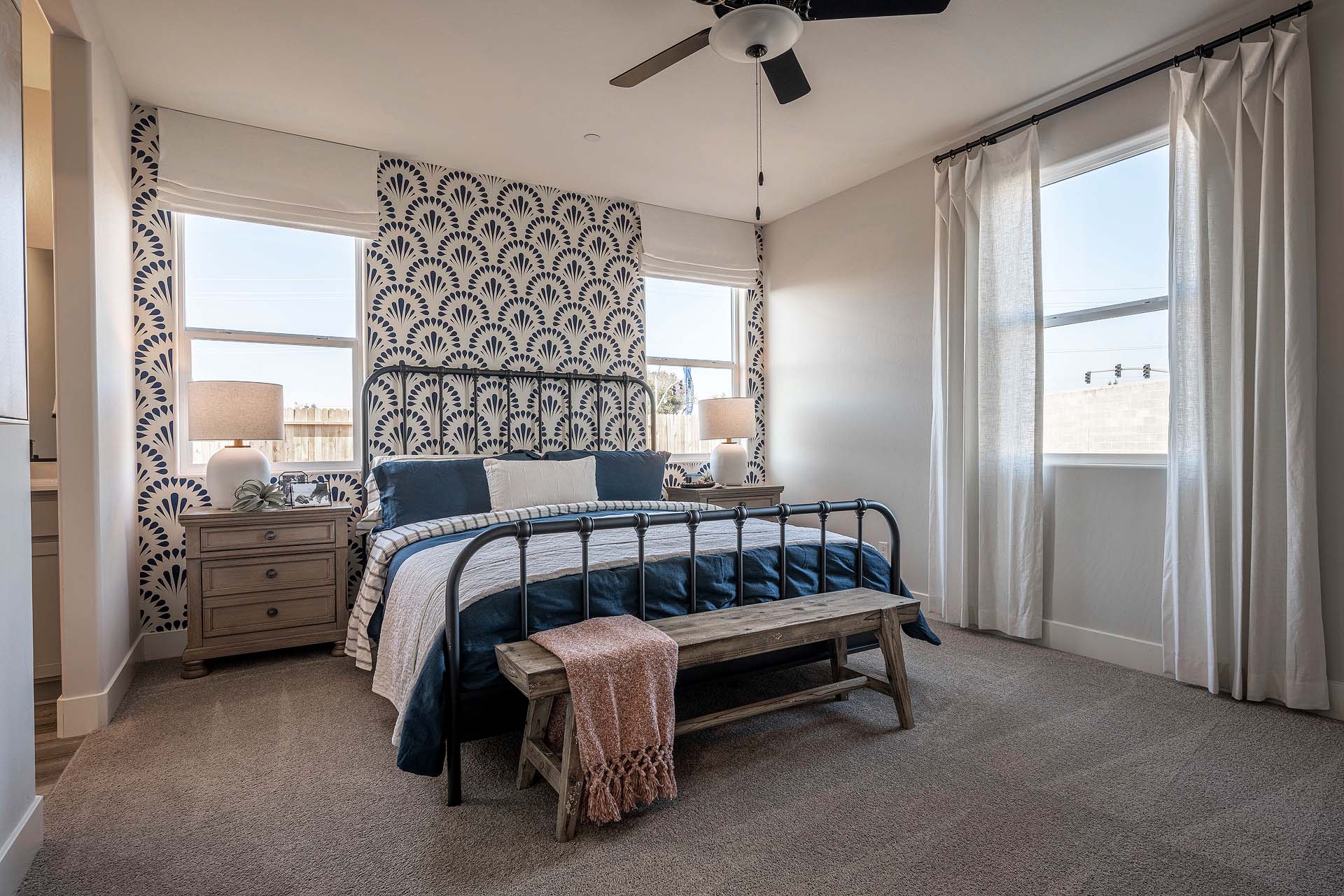 Interior photo of primary suite with bed, end tables, and three large windows.