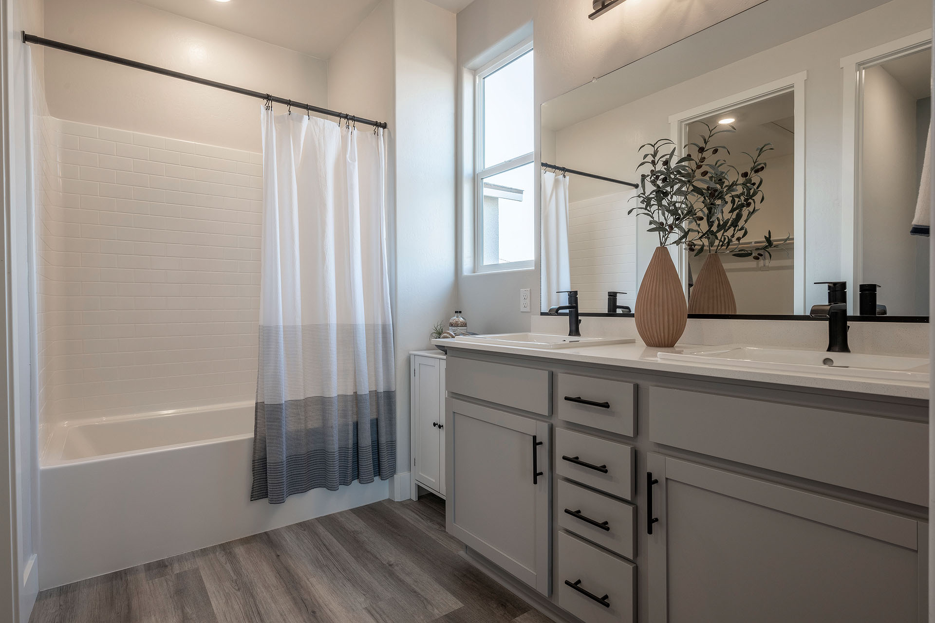 Interior photo of primary bathroom with light gray cabinets, white counter tops, shower, and window.