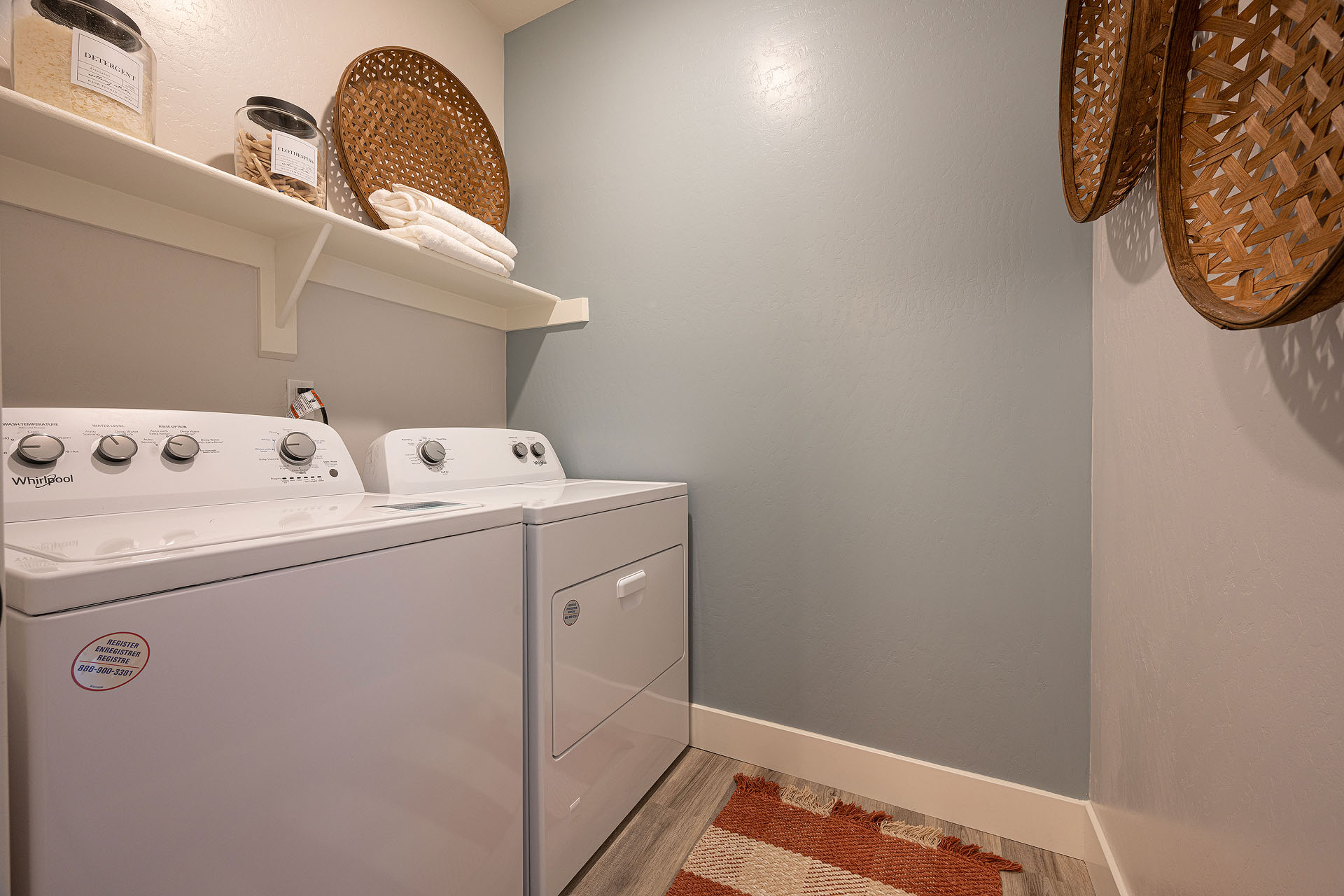 Interior photo of laundry room with washer, dryer, and shelf for storage.