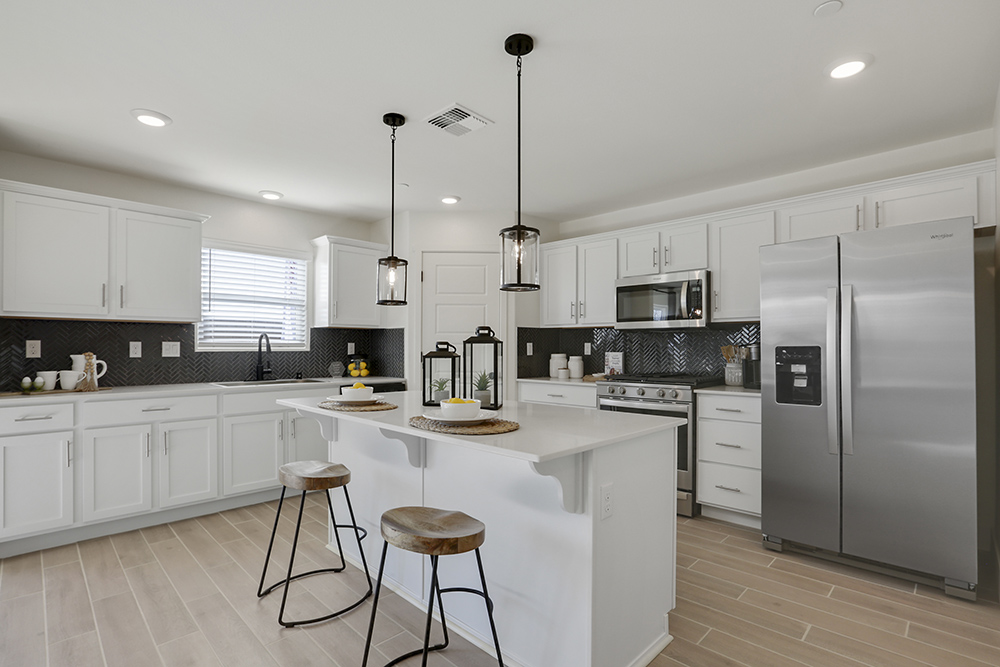Interior photo of kitchen with white cabinets, white countertops, stainless steel appliances, and barstools at kitchen island.