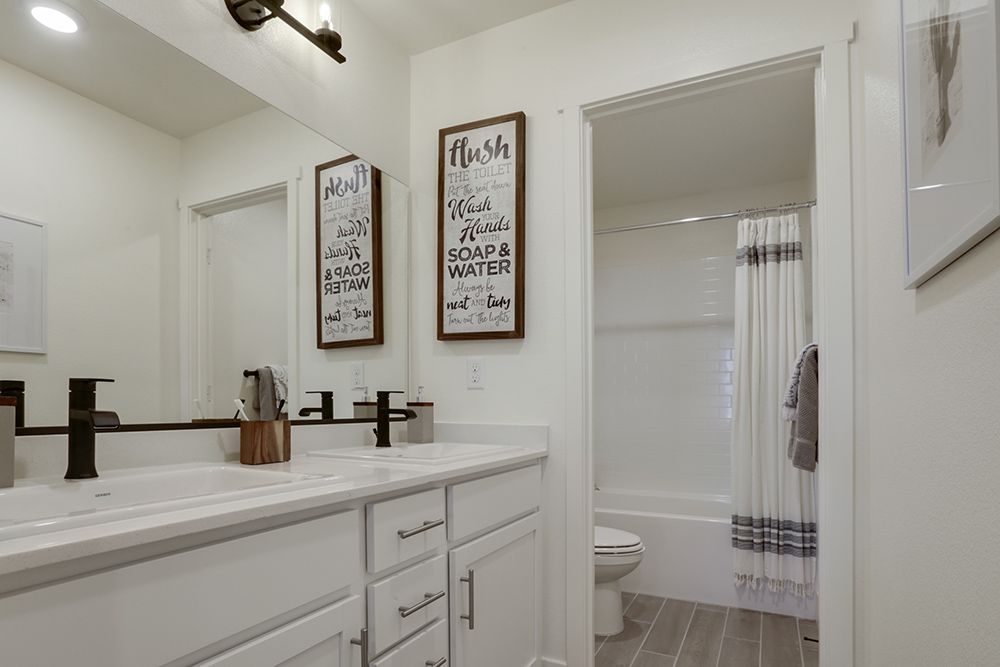 Interior photo of guest bathroom with white cabinets, white countertops, shower, and large mirror.