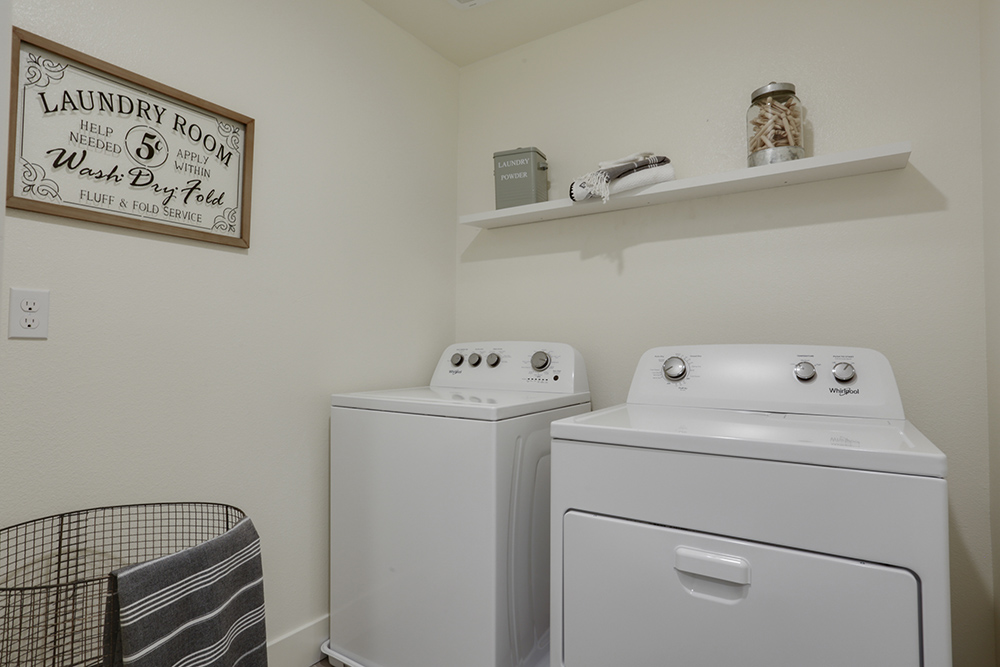Interior photo of laundry room with washer, dryer, and shelf for storage.