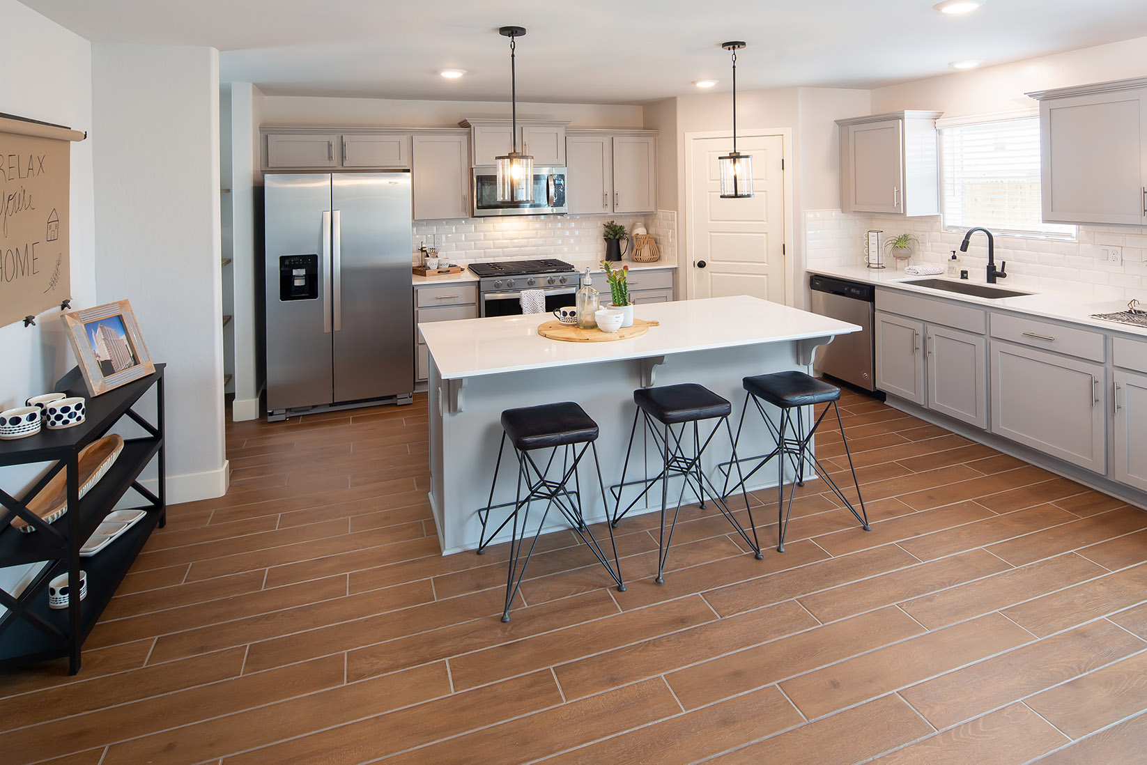 Interior photo of kitchen with light gray cabinets, white countertops, stainless steel appliances, and barstools at kitchen island.