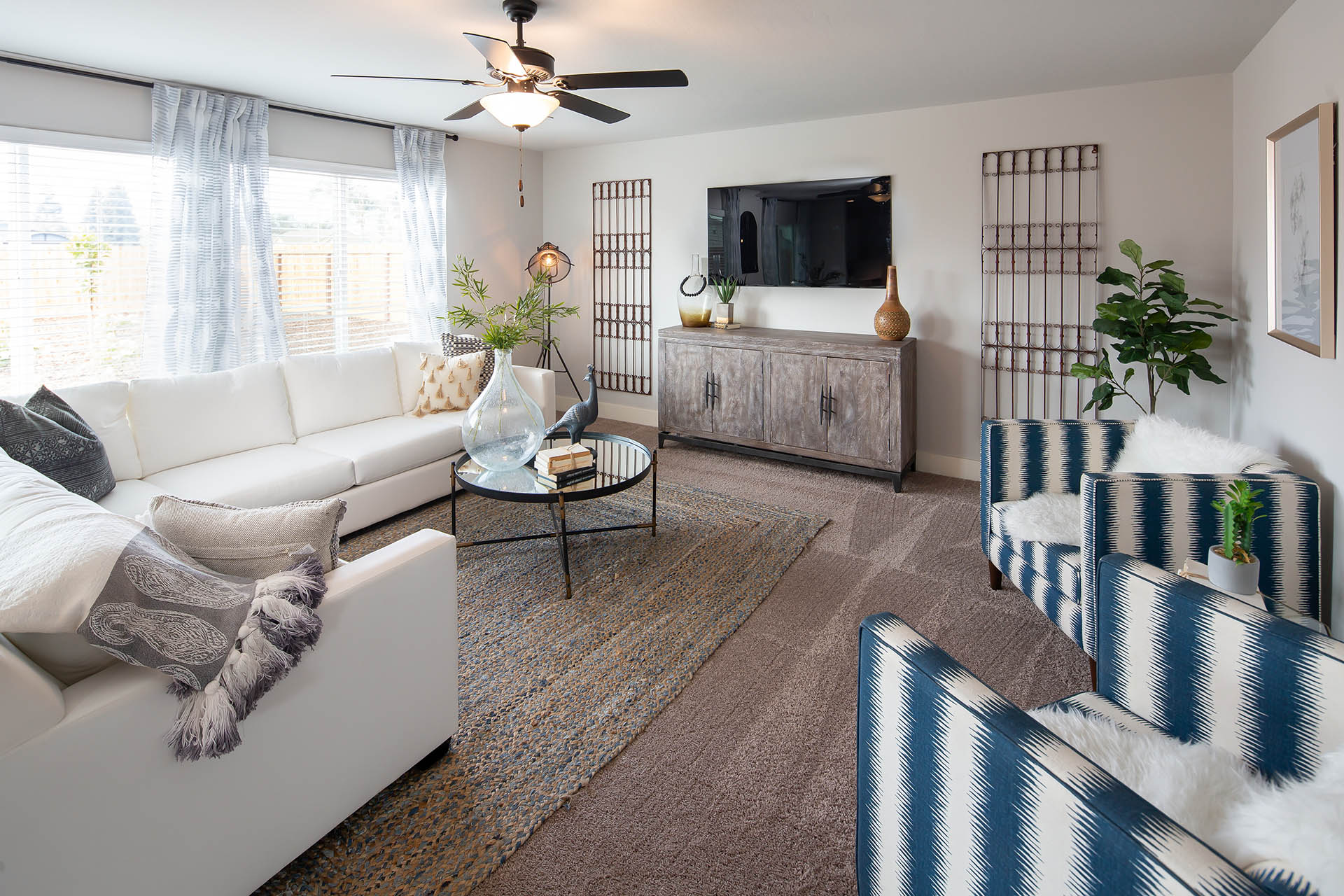 Interior photo of living room with large couch, coffee table, TV, and large windows.
