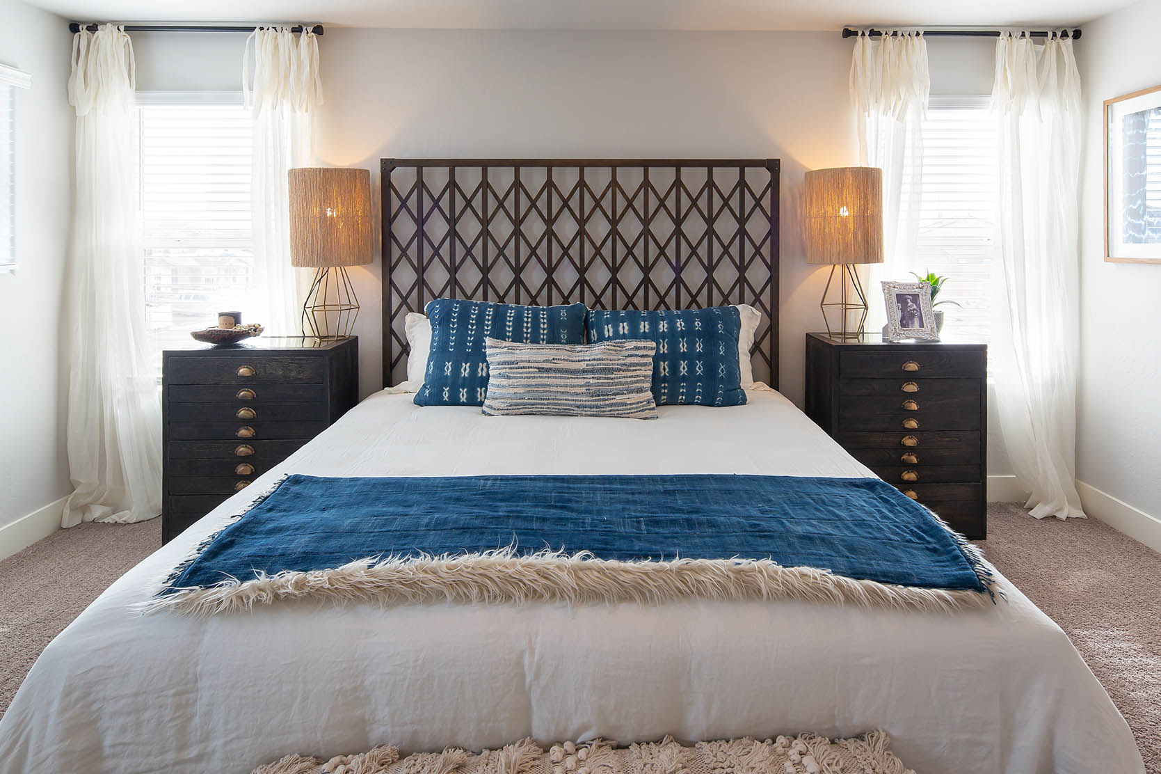 Interior photo of primary suite with bed, end tables, dresser, and large windows.