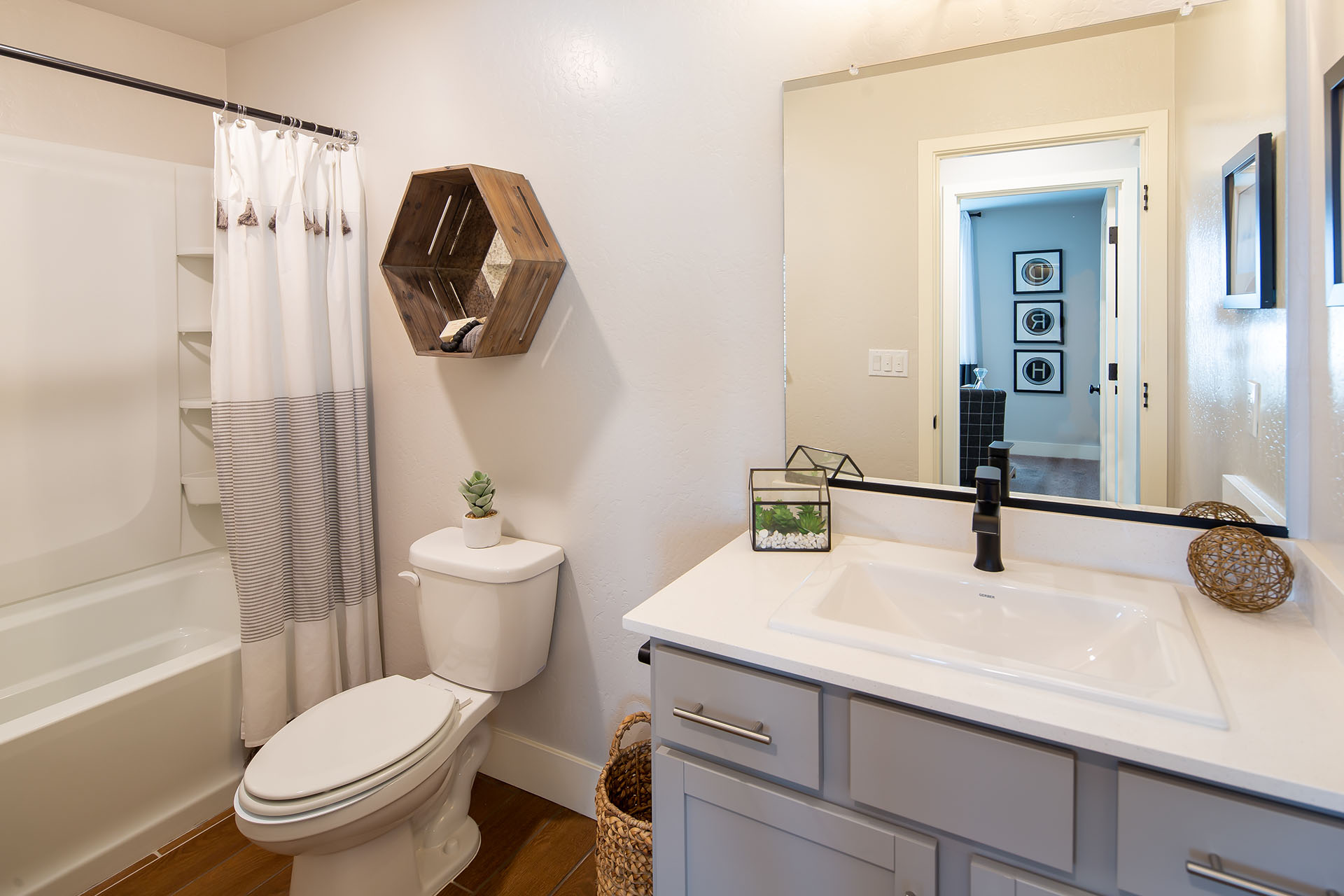 Interior photo of guest bathroom with light gray cabinets, white countertops, shower, and large mirror.