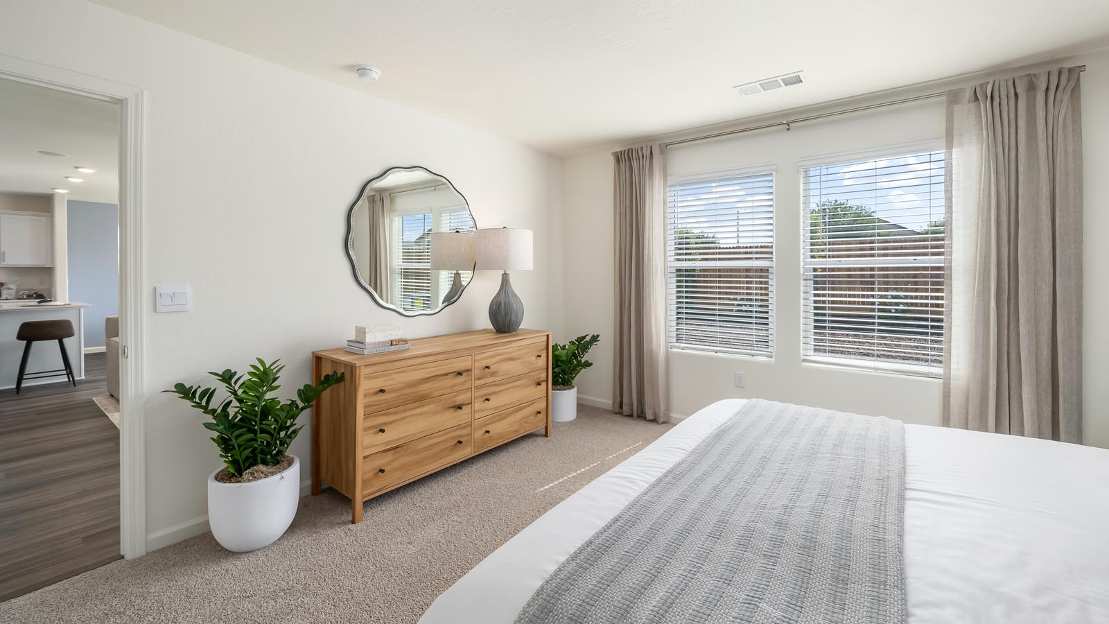 Interior photo of primary bedroom with king size bed, wooden dresser, and large windows