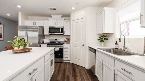 Image of kitchen with white cabinets, white quartz countertops, stainless steel appliances and a walk-in pantry.