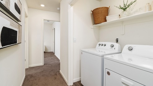Image of a laundry room with a white washer and dryer and shelves on the wall with decor.