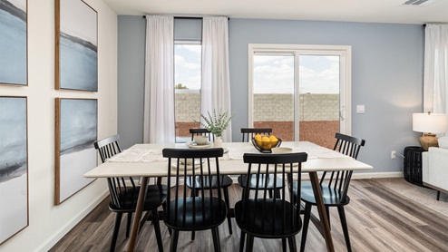 Image of an open concept dining room with a table, chairs, large windows and art on the wall.