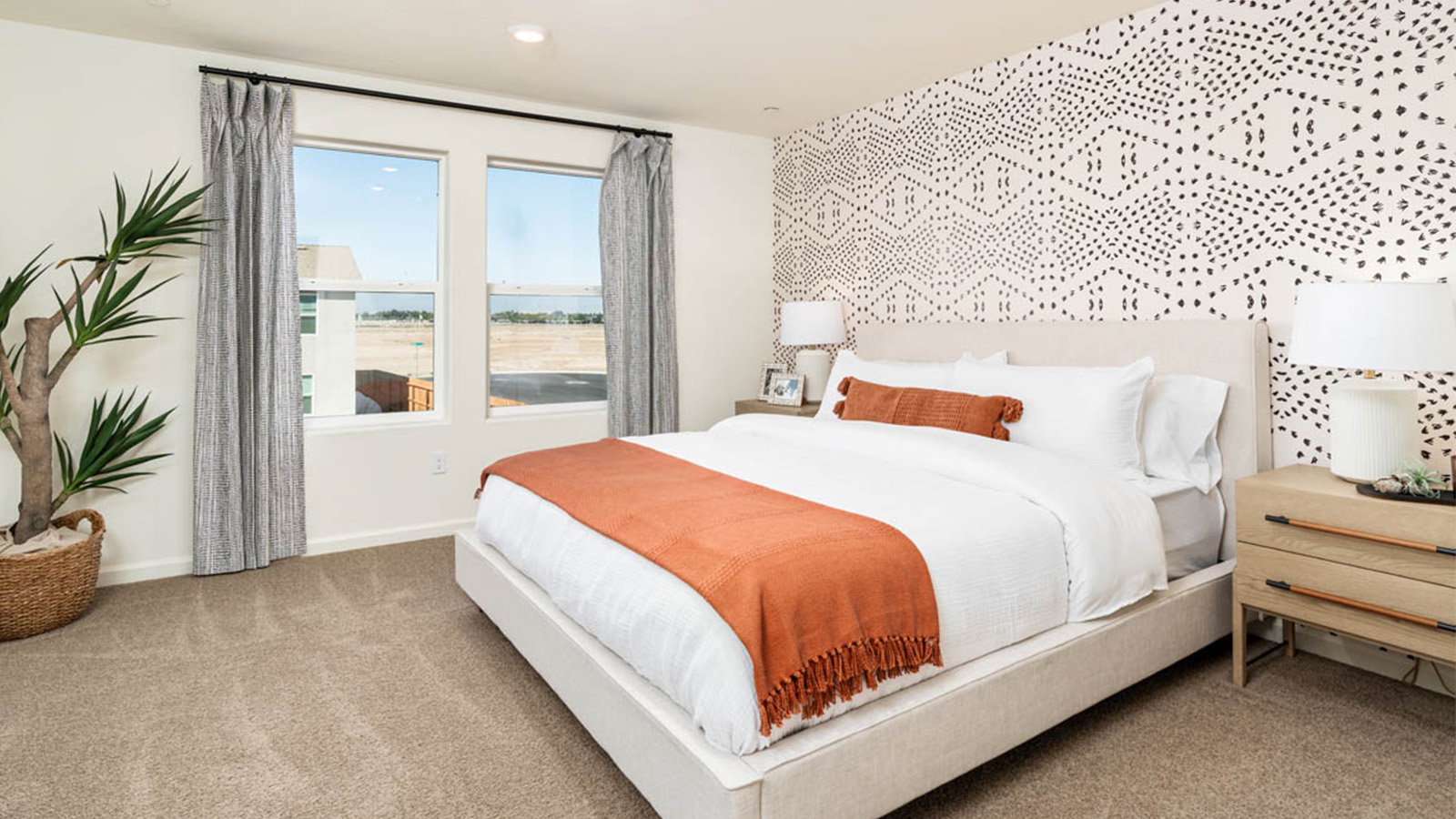 Primary bedroom with a white bed that has orange accents.