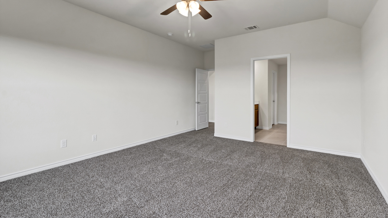 large primary bedroom with carpet and a ceiling fan looking into primary bathroom
