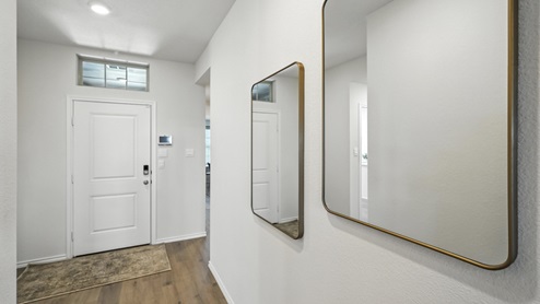 Front entry hallway of the home featuring brown floors, white walls and two mirrors as decor