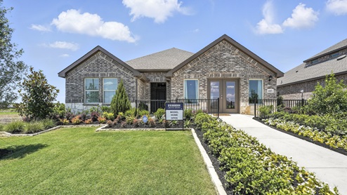 Front exterior of a one story model home with a brick exterior and luscious green landscaping