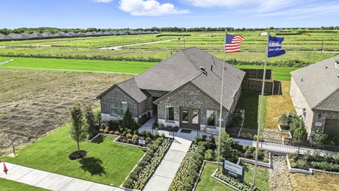 Front exterior of a one story model home with a brick exterior and luscious green landscaping