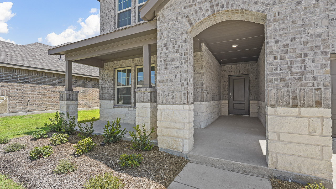 close up of exterior entry of two story home with brick and stone and covered patio and porch