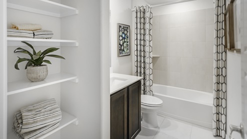 Bathroom with white tub and a vanity with brown cabinets and shelves for storage