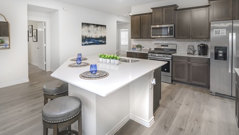Large kitchen with island surrounded by brown cabinets and hard surface countertops and stainless steel appliances