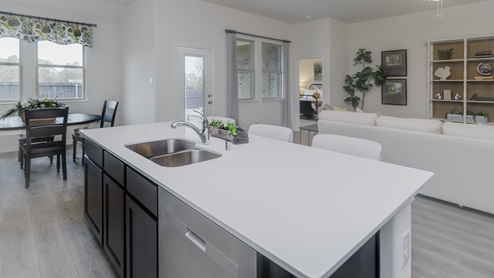 Kitchen with island surrounded by brown cabinets with hard surface countertops and stainless steel appliances and views into the dining area