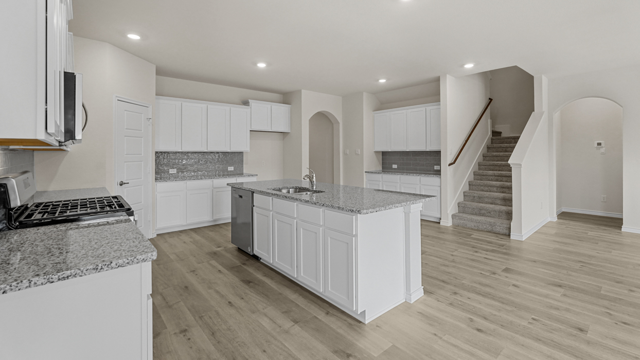 large kitchen with white cabinets and granite countertops next to stairs