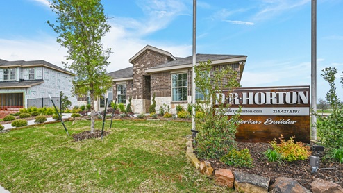 A one-story model home with stone at the bottom of the elevation and brown brick. Photo also shows a wooden D.R. Horton sign