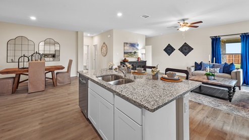 Open-concept kitchen with stainless steel appliances and a large island and white cabinets. Photo also shows the large living room
