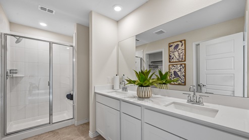 A large primary bathroom with walk in shower and extended vanity with white cabinets