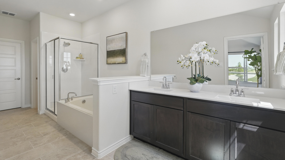 primary bathroom with light colored floors dark cabinets and white counters