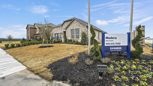 Madera sales model office with light brown brick and landscaping around sidewalk next to community signage