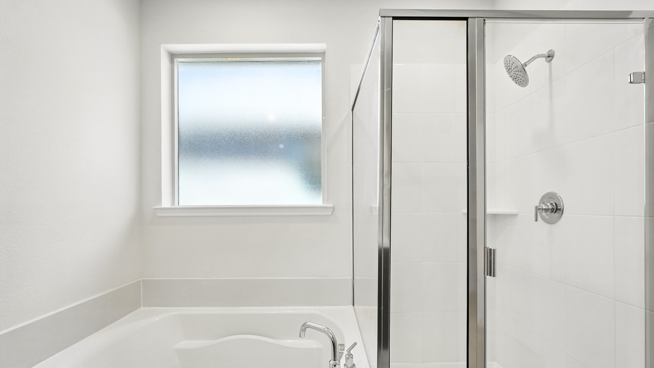 Primary bathroom tub with glass shower door next