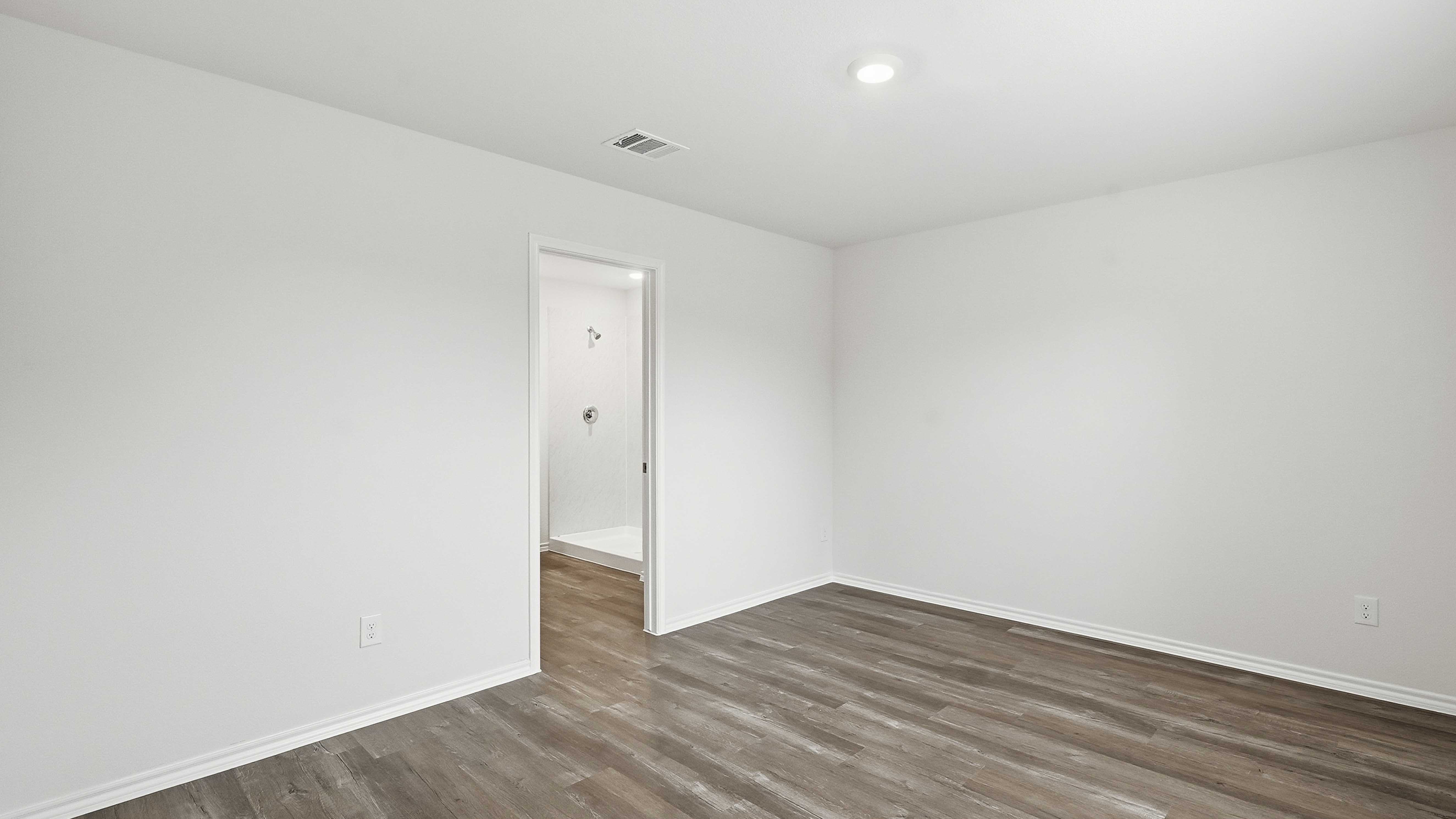 primary bedroom with hardwood floors white walls and large windows providing natural light